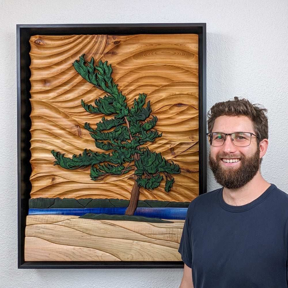 Alex Jepson standing beside The Windswept Pine wood sculpture, highlighting the natural beauty and fine craftsmanship of the tree artwork.
